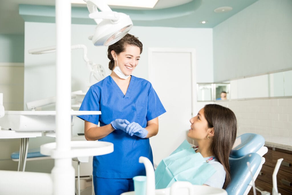 smiling dentist in uniform talking to girl at clinic
